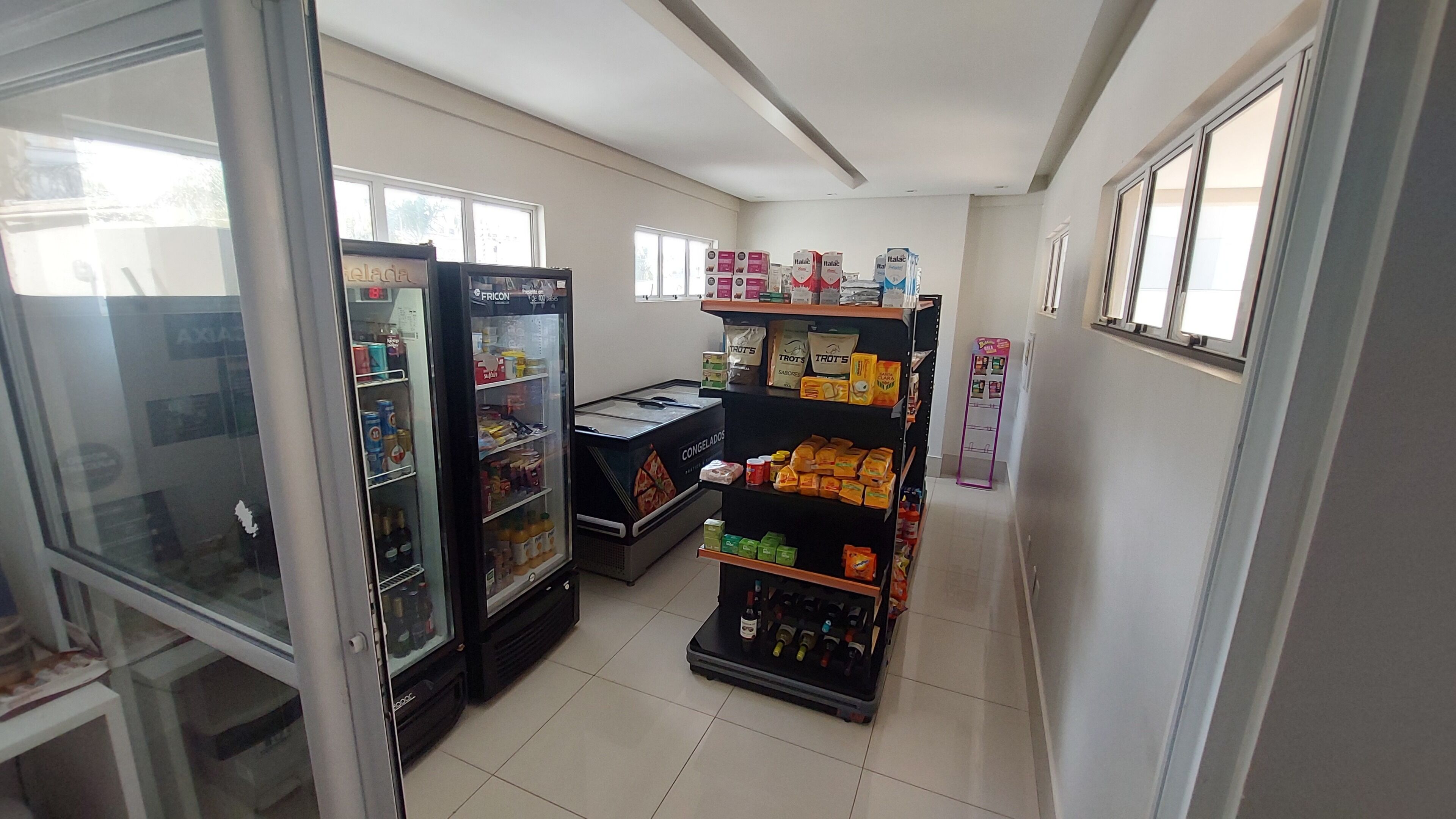 A narrow hallway with a refrigerator stocked with beverages, a freezer, and shelves with packaged goods.