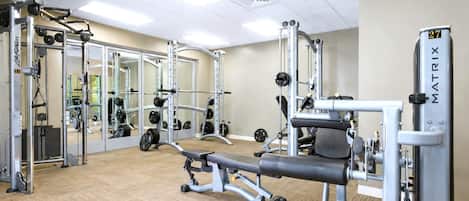 Une salle de sport équipée de divers appareils d’exercice, notamment un banc de développé couché, des machines de musculation et des poids libres.