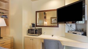 Una habitación de hotel con cama, escritorio con computadora, microondas, lámpara y televisión.