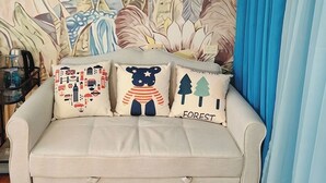 A beige sofa with three decorative pillows against a floral-patterned wall. - Blue Bunny-Eared Stay | Ocean View | 2min to Beach (Surfers Paradise)