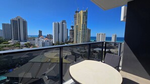 Ein Balkon mit Tisch und Stühlen, der auf eine Stadt mit Hochhäusern und blauem Himmel blickt.