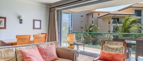 Quarto de hotel com varanda, ventoinha no teto, sofá, uma cadeira e uma mesa.