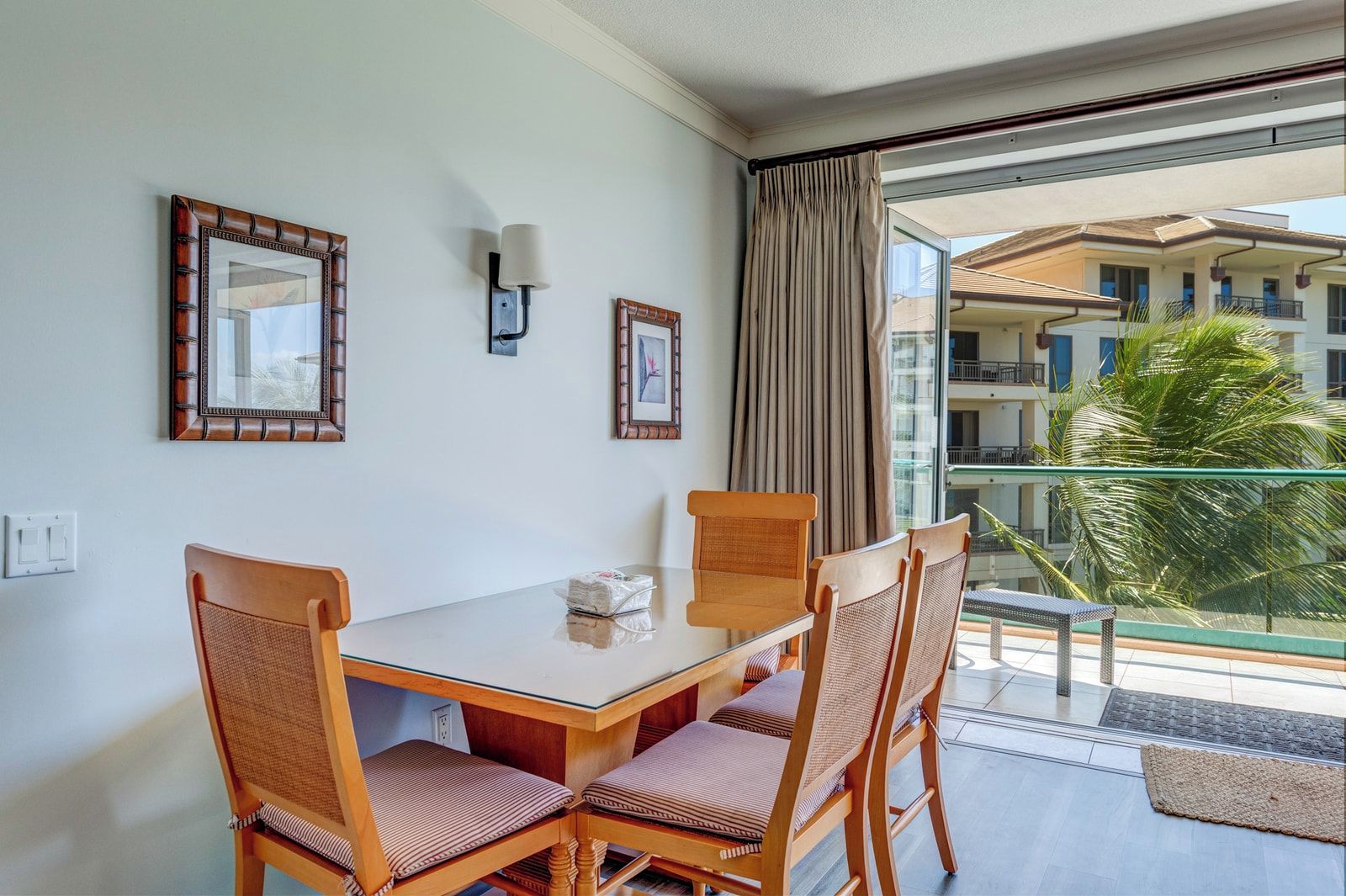 Une chambre d’hôtel avec un balcon, une table à manger avec des chaises et deux tableaux encadrés au mur.
