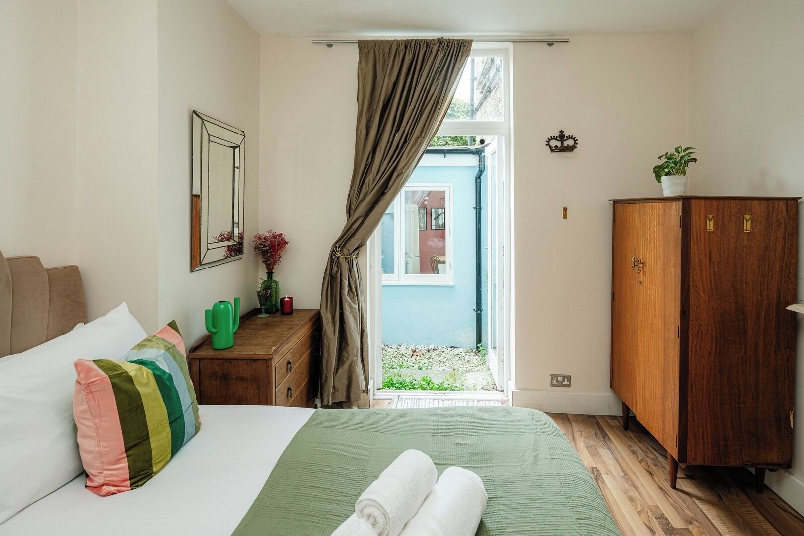 A bedroom with a bed, a wooden dresser, a mirror, a window with curtains, and a view of the outside.