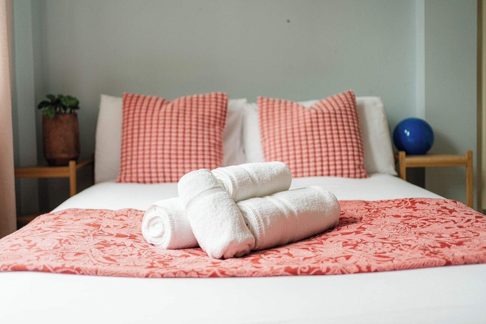 Cama bem arrumada com toalhas brancas dobradas, colcha estampada em rosa e almofadas combinando.