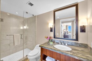 A modern bathroom with a glass shower enclosure, a white toilet, a marble sink, and a large mirror. - KBM Resorts | 4 FREE CARS | Honua Kai Hokulani | Ocean view | 7-Bedroom Multi-Unit Listing,  Recently Updated, Sunsets! ML-2957 (Lahaina)