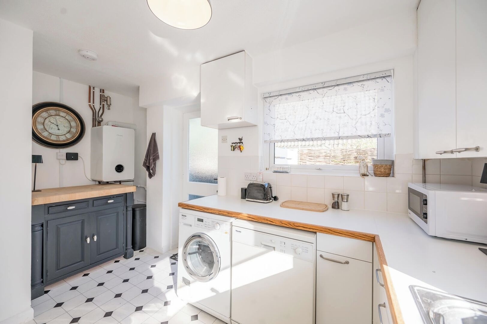 Een kleine keuken met een wasmachine, een magnetron en een raam met uitzicht.