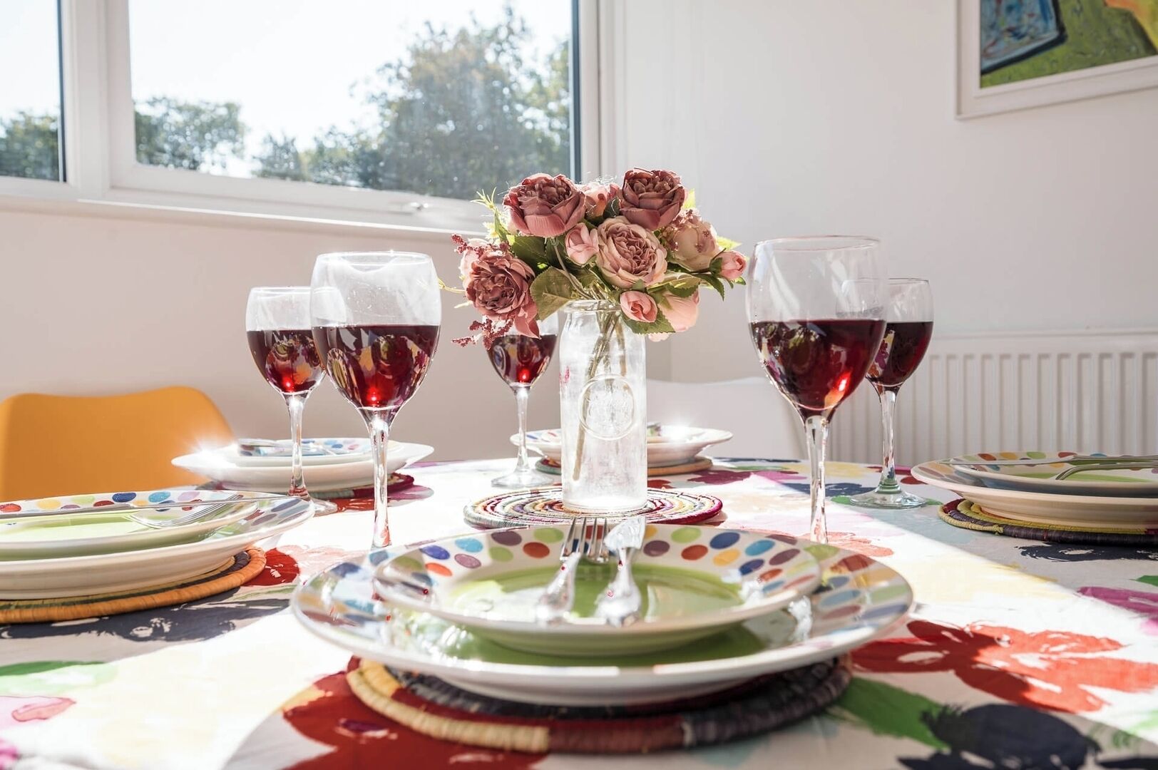 A dining table with plates, glasses, and a vase of flowers.