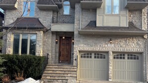 A two-story house with a stone facade, a front entrance with steps, and two garage doors. - Cozy Room 202 | Private Bathroom | Free Parking | Easy Transit (Toronto)