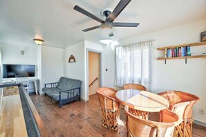 Un salon comprenant un téléviseur, un canapé, une table à manger avec des chaises, un ventilateur de plafond et une bibliothèque.