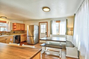 A kitchen with wooden cabinets, a stainless steel refrigerator, a dining table, and a window with curtains. - The Cottage on Colorado (Buena Vista)