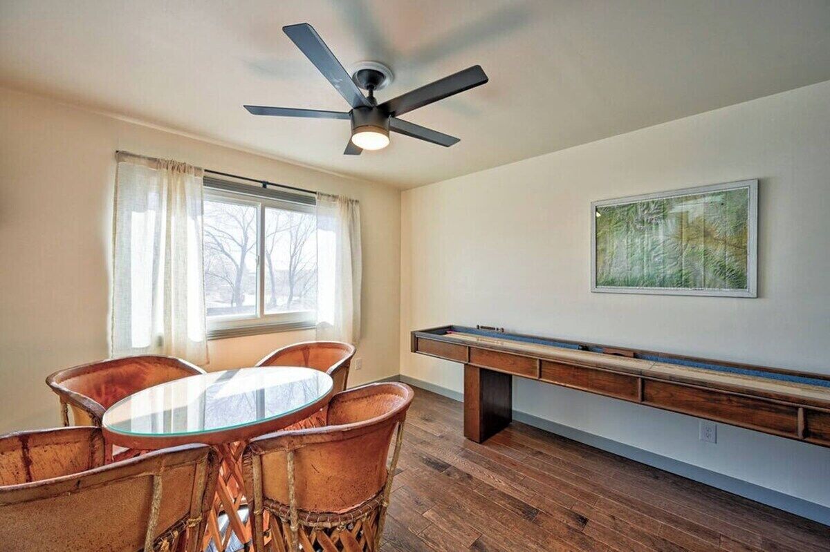 A room with a pool table, a ceiling fan, a dining table with chairs, and a window with curtains.
