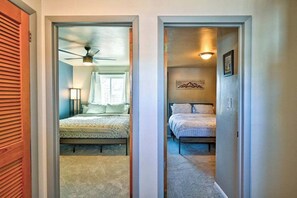 Un couloir mène à deux chambres, chacune étant équipée d’un lit, d’un ventilateur de plafond et d’une lampe fixée au mur.