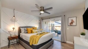 A modern bedroom with a bed, bedside table, lamp, ceiling fan, and a view to the outside. - The PALMERA House with Private Pool Oasis, 3BR, Near Galleria Sacramento (Sacramento)