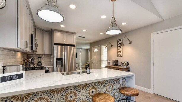 A modern kitchen with a marble countertop, stainless steel appliances, and a bar area with stools. - The PALMERA House with Private Pool Oasis, 3BR, Near Galleria Sacramento (Sacramento)