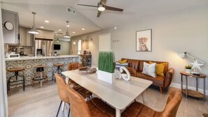 A modern kitchen with a dining area, a ceiling fan, and a living room with a sofa and a painting. - The PALMERA House with Private Pool Oasis, 3BR, Near Galleria Sacramento (Sacramento)
