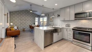A modern kitchen with a central island, stainless steel appliances, and a dining area with a brown leather couch. - The PALMERA House with Private Pool Oasis, 3BR, Near Galleria Sacramento (Sacramento)