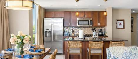 A modern kitchen with stainless steel appliances, a central island, and a dining area with a table set for two.