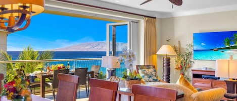 Una habitación de hotel con balcón, zona de comedor, sofá y televisión.