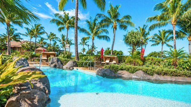 Une piscine d’hôtel bordée de palmiers, avec des chaises longues et un ciel d’un bleu limpide.