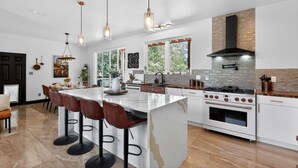 Une cuisine moderne dotée d’un îlot central, de tabourets de bar, de luminaires suspendus et d’une grande cuisinière.