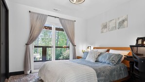 Une chambre avec un grand lit, un bureau, une chaise et une vue sur la verdure par la fenêtre.