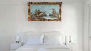 Un dormitorio con una cama, dos mesitas de noche, un cuadro y una puerta.