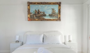 A bedroom with a bed, two bedside tables, a painting, and a door. - KozyGuru | MacMahons Point | Harbour Breeze Escape (McMahons Point)