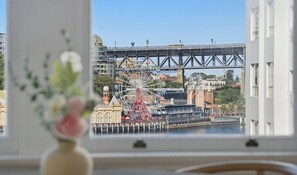 A view of a Ferris wheel and a bridge from a window with a vase of flowers on the table. - KozyGuru | MacMahons Point | Harbour Breeze Escape (McMahons Point)