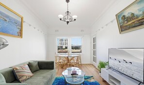 A living room with a sofa, a glass coffee table, a TV, and a dining area with chairs and a table. - KozyGuru | MacMahons Point | Harbour Breeze Escape (McMahons Point)