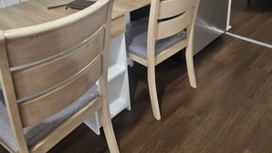 A kitchen with a wooden table and two chairs, a stainless steel refrigerator, and white cabinets.