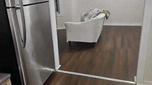 A compact kitchen with a stainless steel refrigerator, a white chair, and a wooden floor.
