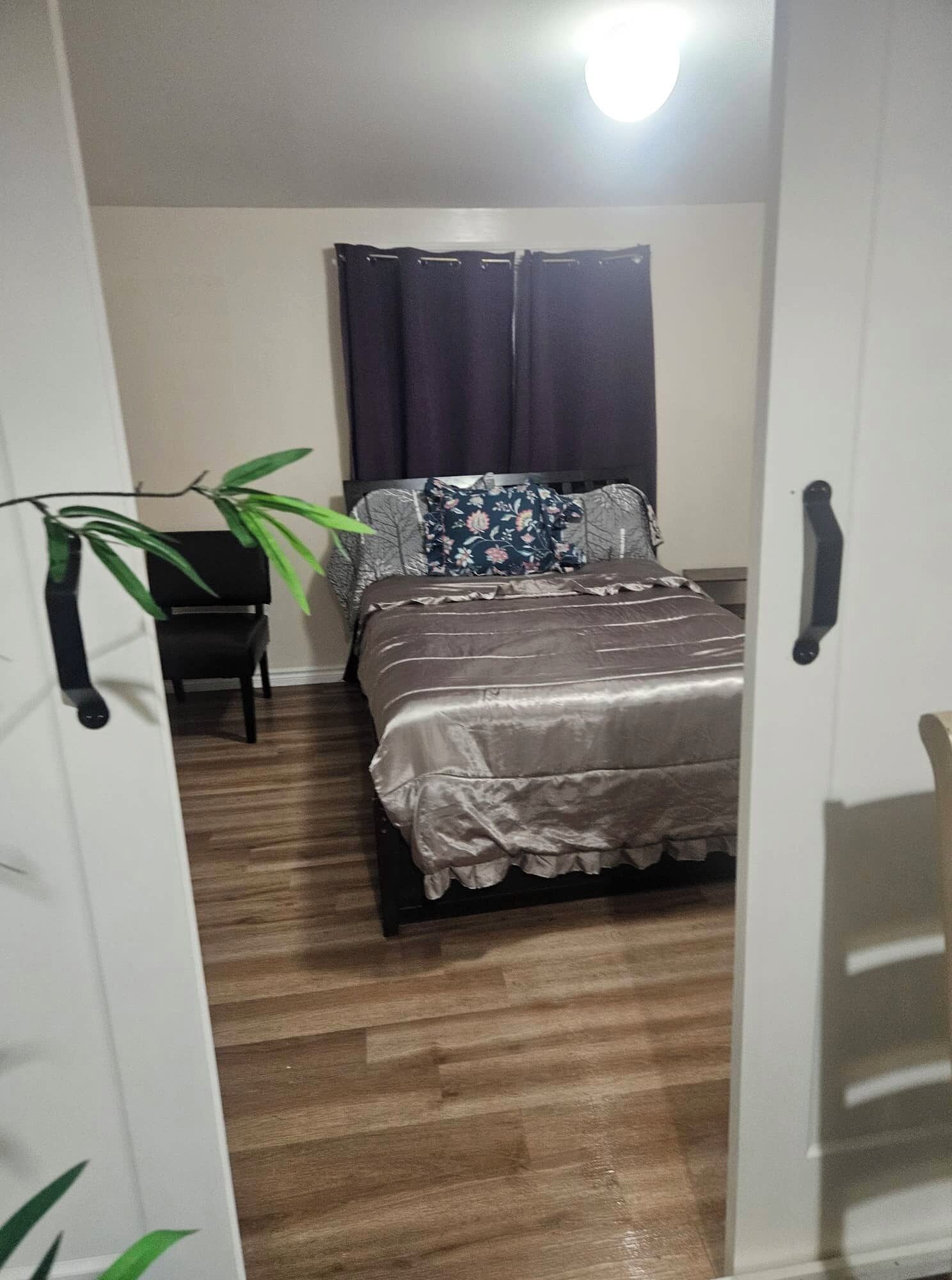 Ein Schlafzimmer mit Bett, Sessel, Pflanze und einem Fenster mit Vorhängen.
