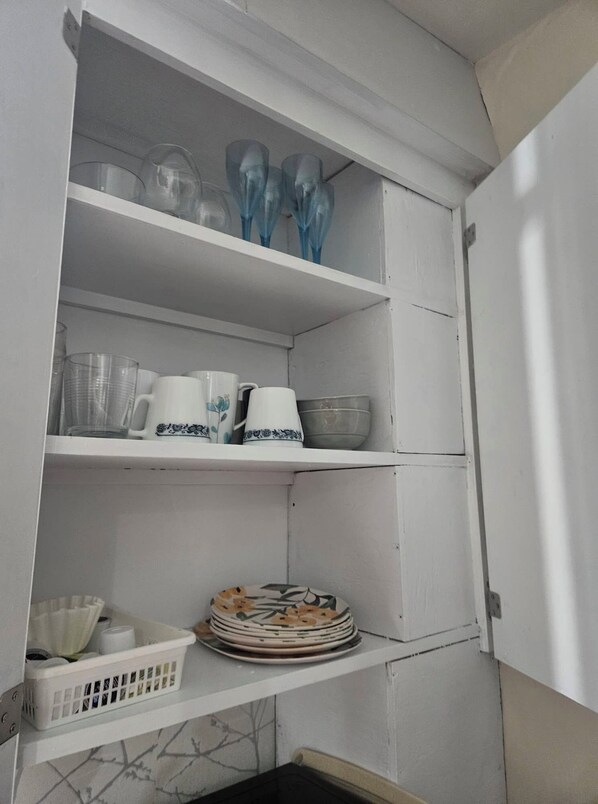 A kitchen cabinet with shelves containing glassware, cups, and plates.