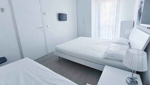 Et moderne hotelværelse med en enkelt seng, et natbord med lampe, et garderobeskab og et stort spejl.