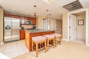 A modern kitchen with stainless steel appliances, a central island with bar stools, and a large window. - 2 Honua Kai Villas | Ocean Front | Sleeps 14 | Free Car w/ 6+ Nights | ML-3074 (Lahaina)
