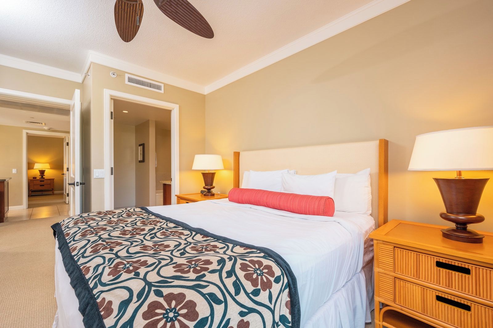 Habitación de hotel con una cama, dos mesitas de noche con lámparas, una puerta que da al baño y un pasillo con una lámpara.