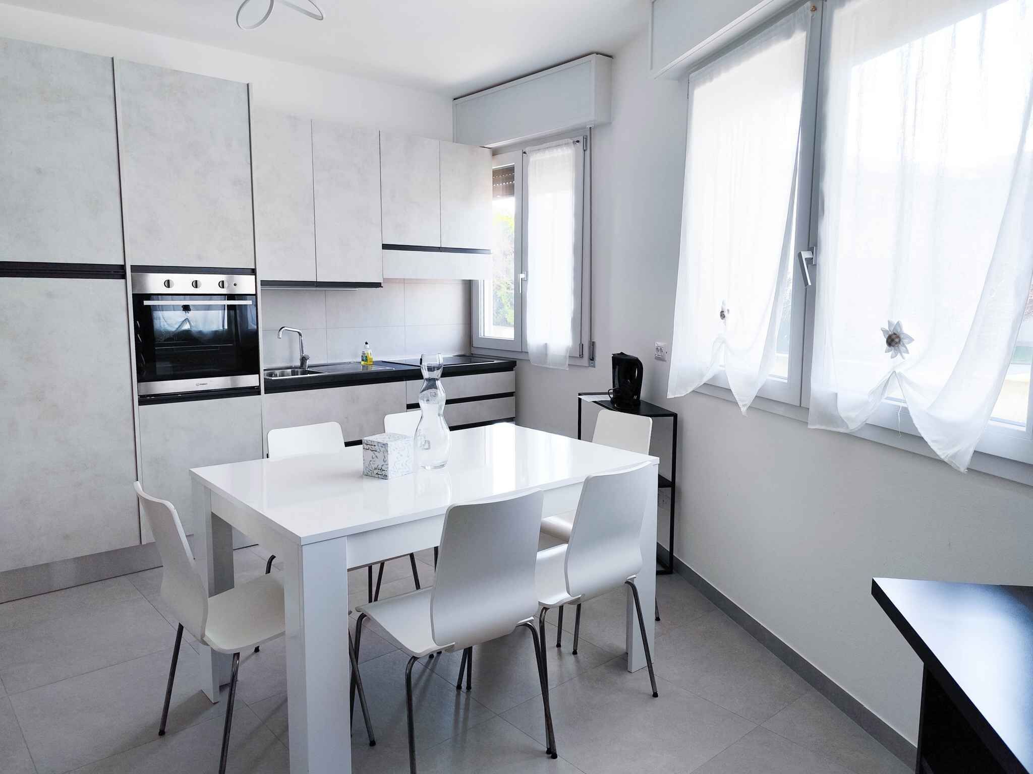 Cozinha moderna com armários brancos, forno embutido, pia e área de jantar com mesa e cadeiras brancas.