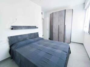 A bedroom with a bed, a wardrobe, and a wall-mounted shelf. - Holiday apartment with pool (Cavallino-Treporti)