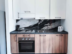 A modern kitchen with white cabinets, a marble backsplash, a gas stove, a coffee maker, and a kettle. - Holiday apartment with pool (Cavallino-Treporti)