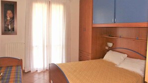 Een slaapkamer met een bed, een houten garderobe, een raam met gordijnen en een radiator.