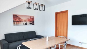 Een moderne woonruimte met een bank, eettafel, stoelen, een televisie en een schilderij aan de muur.