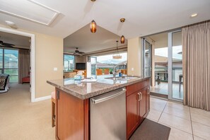 A modern kitchen with a granite countertop, stainless steel appliances, and a sliding glass door leading to a balcony. - Honua Kai | Ocean View 4 BR, Sleeps 12 | Car Incl. w/ 6+ Nights | HKH ML-3077 by KBM (Lahaina)