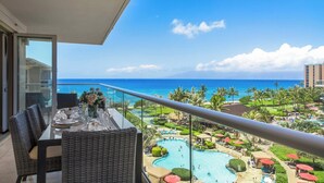 Ein Balkon mit Esstisch, Stühlen und Blick auf einen Hotelpool und den Ozean.