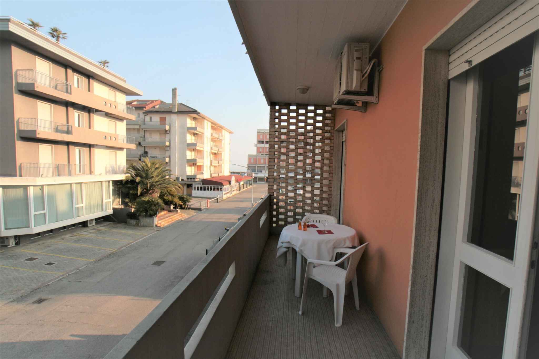 A balcony with a table and chairs, a decorative fence, and a view of neighboring buildings.