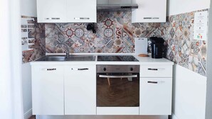 Eine kleine Küche mit weißen Schränken, einer Edelstahl-Spüle und einer dekorativen Spritzschutzwand.