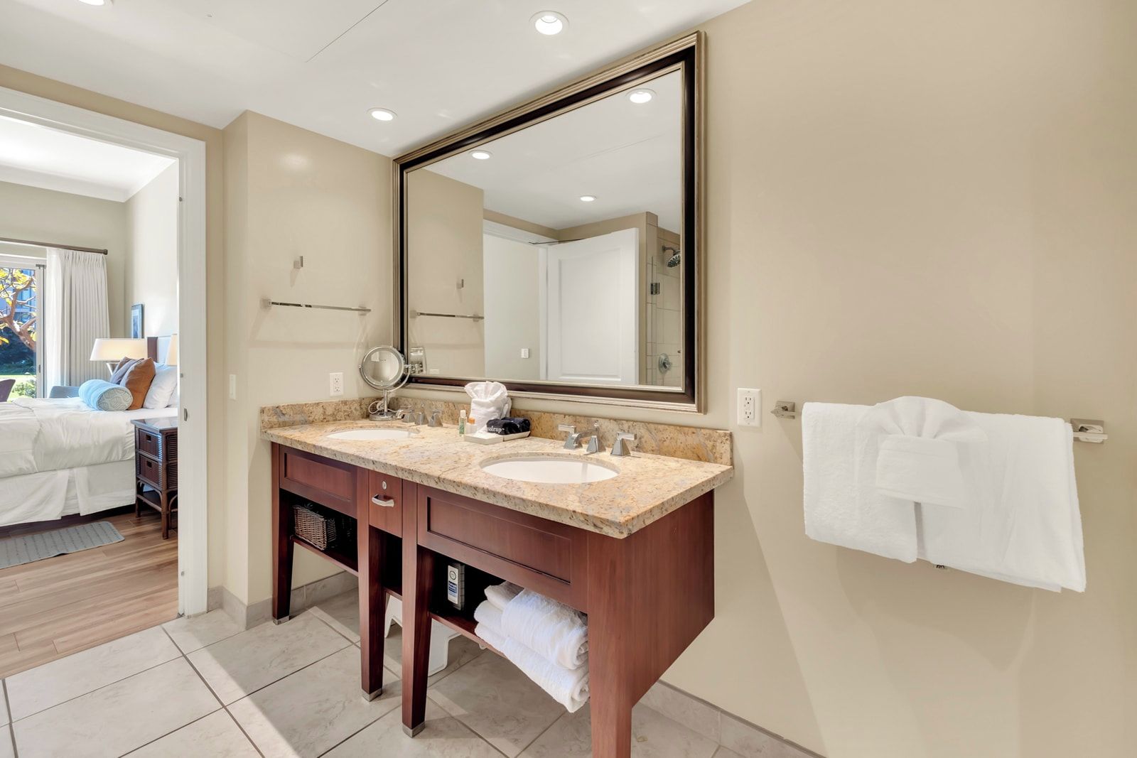 A hotel bathroom with two sinks, a large mirror, and a towel rack.