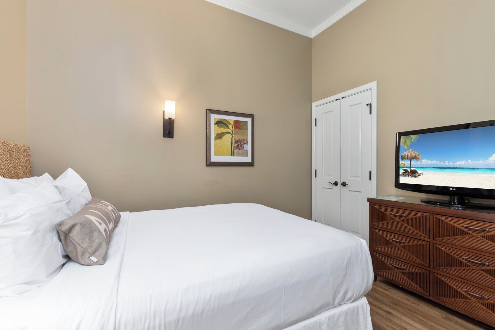 Une chambre d’hôtel avec un lit, un téléviseur posé sur une commode en bois, un tableau encadré au mur et une porte.