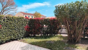 A paved walkway, a hedge with red foliage, and a tree with green leaves. - Holiday apartment with balcony (Cavallino-Treporti)