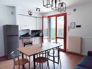 A compact kitchen with a dining area, a refrigerator, a stove, and a window with a view of greenery. - Holiday apartment with pool (Cavallino-Treporti)